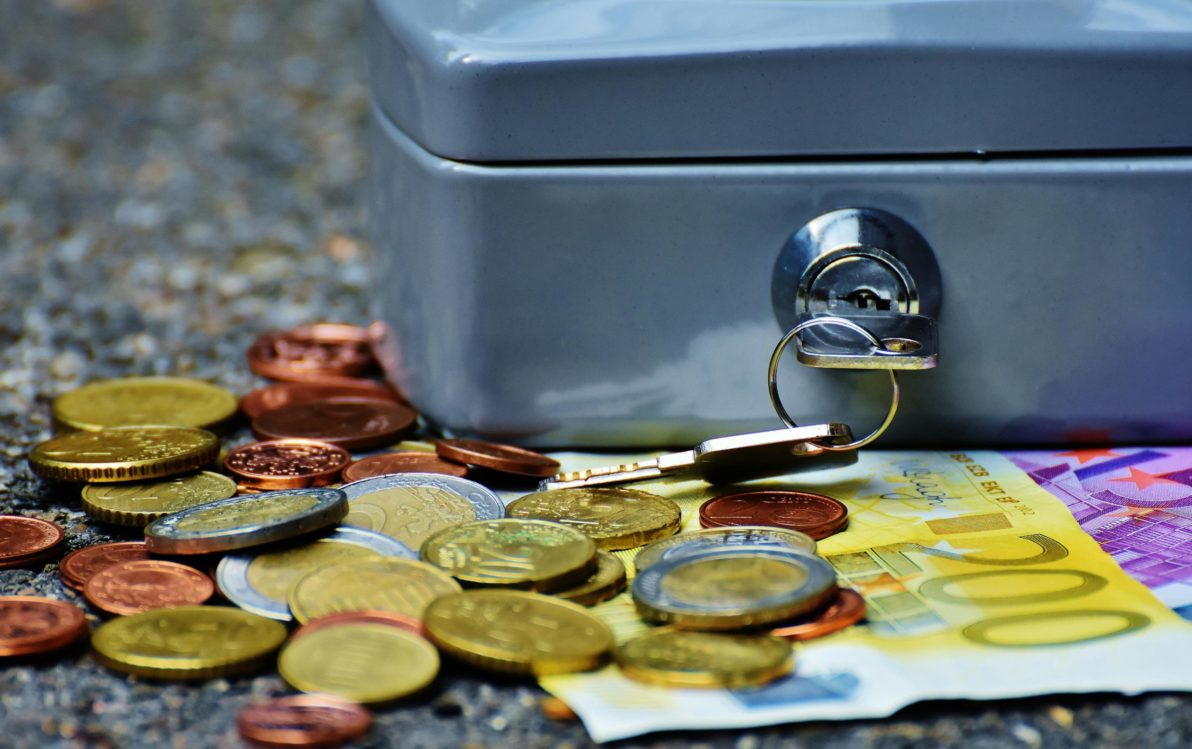 Una caja de efectivo cerrada con monedas de euro dispersas y un billete de 200 euros.